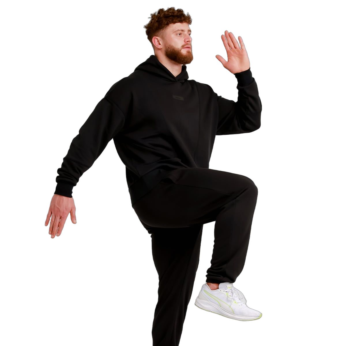 Uomo in pantaloni da jogging neri e felpa con cappuccio, solleva una gamba.