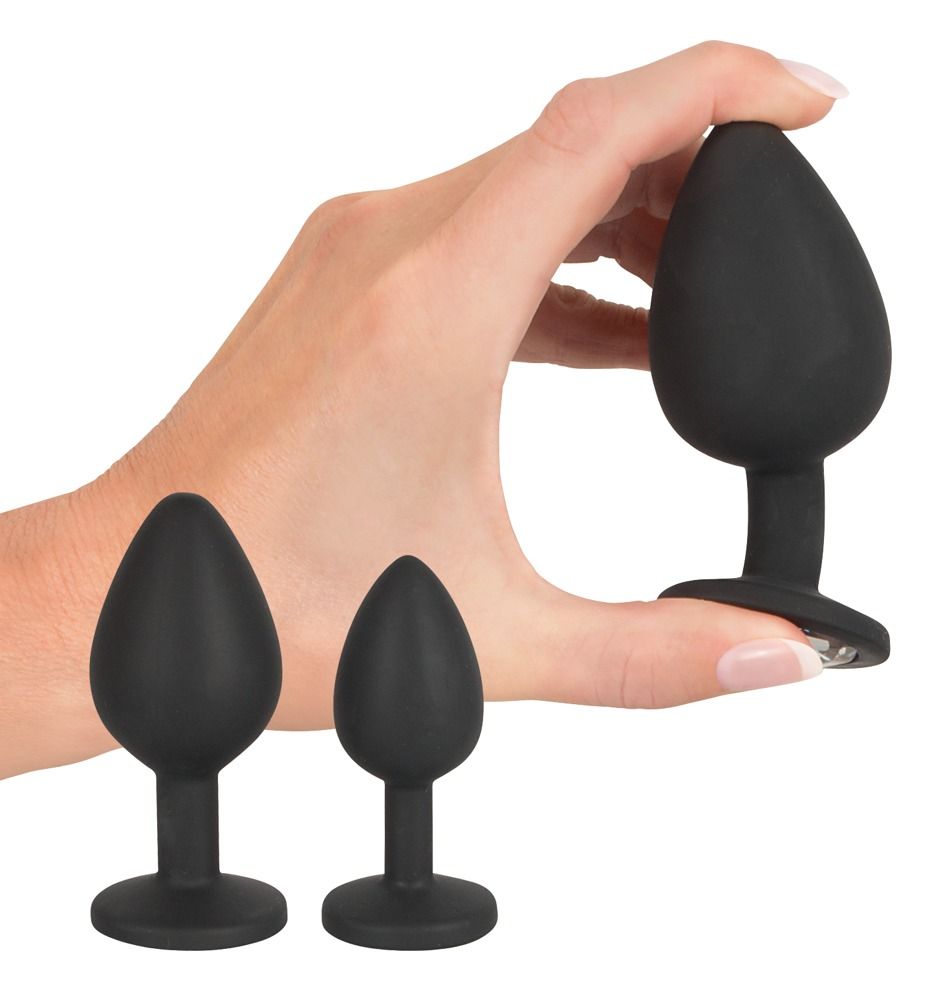 Mano che tiene un plug anale nero. Altri due plug accanto. Tutti in silicone.