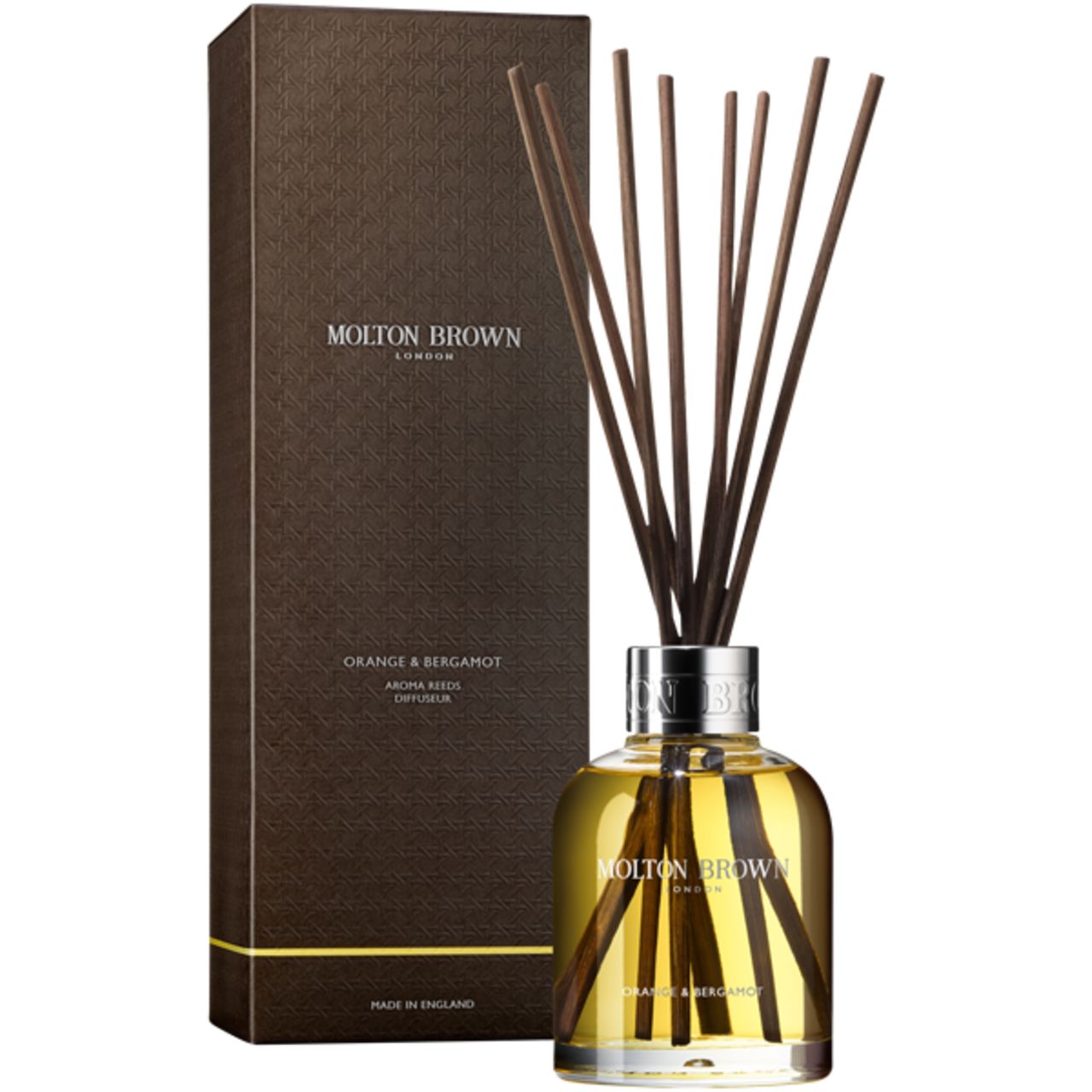 Confezione del prodotto con bastoncini profumati. Bastoncini marroni che escono da un flacone. Scritta: Molton Brown, Orange & Bergamot. Scatola marrone accanto.