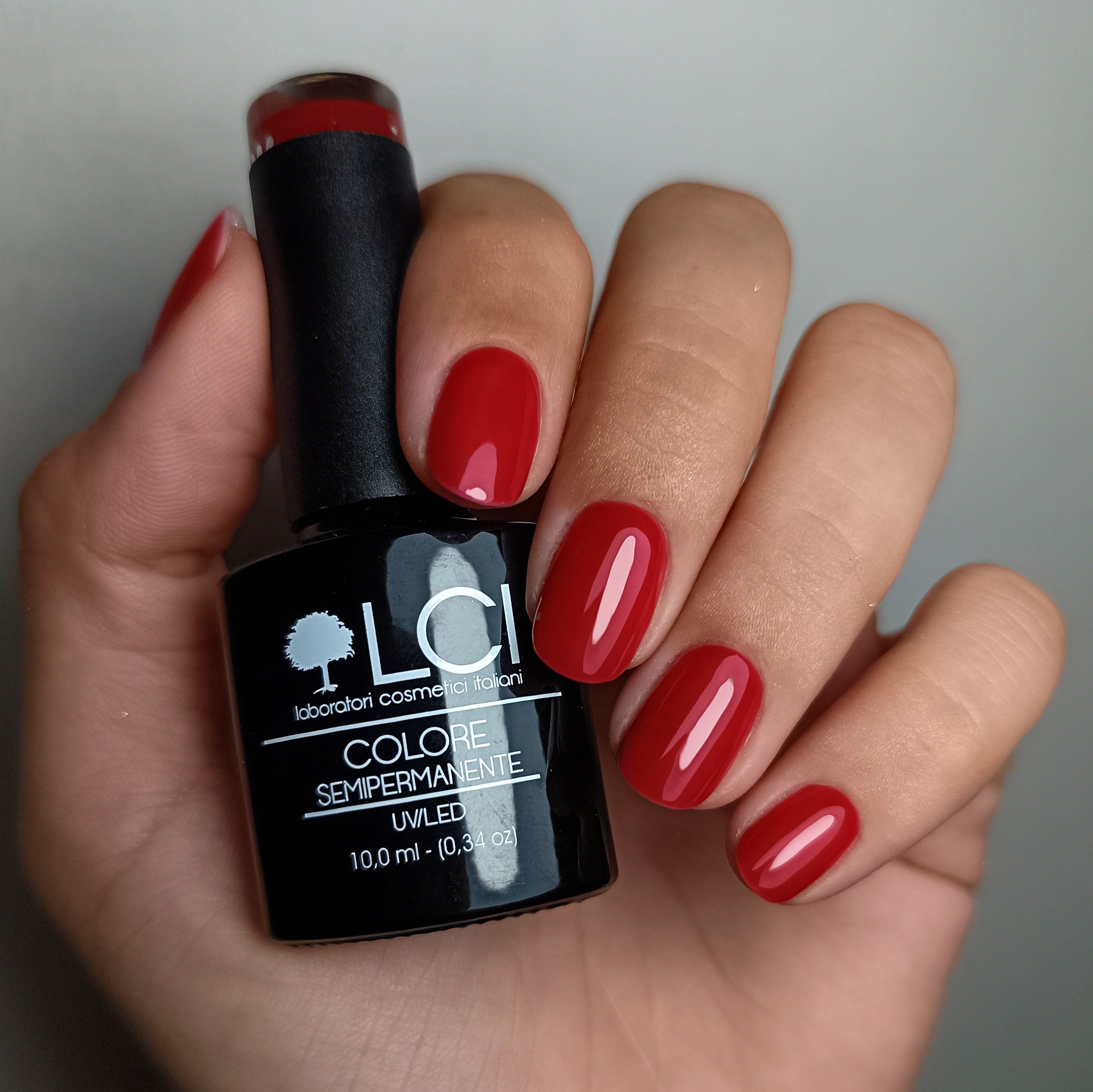 Mano con unghie rosse smaltate e flacone di smalto. Scritta: LCI, Colore Semipermanente, UV/LED.