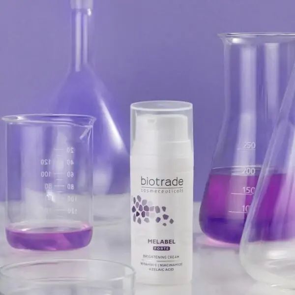 Flacone bianco di crema Biotrade Melabel Forte con dosatore. Testo: Melabel Forte, Brightening Cream, Vitamina C, Niacinamide, Acido Azelaico. Materiale da laboratorio.