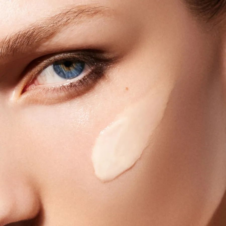 Primo piano di un viso. Sulla pelle è applicata una crema color crema.