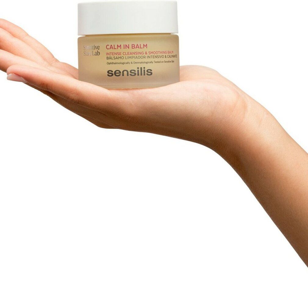 Mano che tiene un vasetto di crema con coperchio bianco. Scritta: CALM IN BALM, sensilis. Per pelli sensibili. Balsamo detergente intenso.