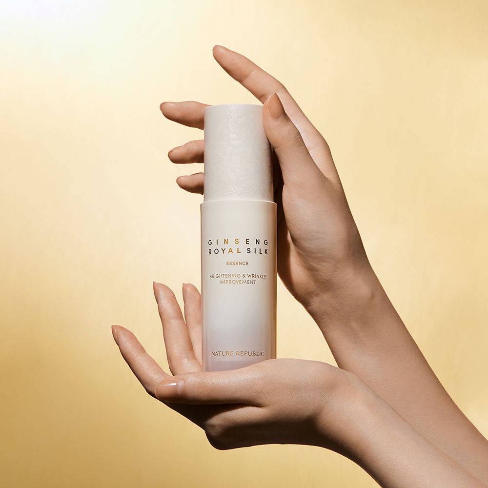 Flacone bianco Ginseng Royal Silk Essence tenuto in mano. Sfondo dorato.
