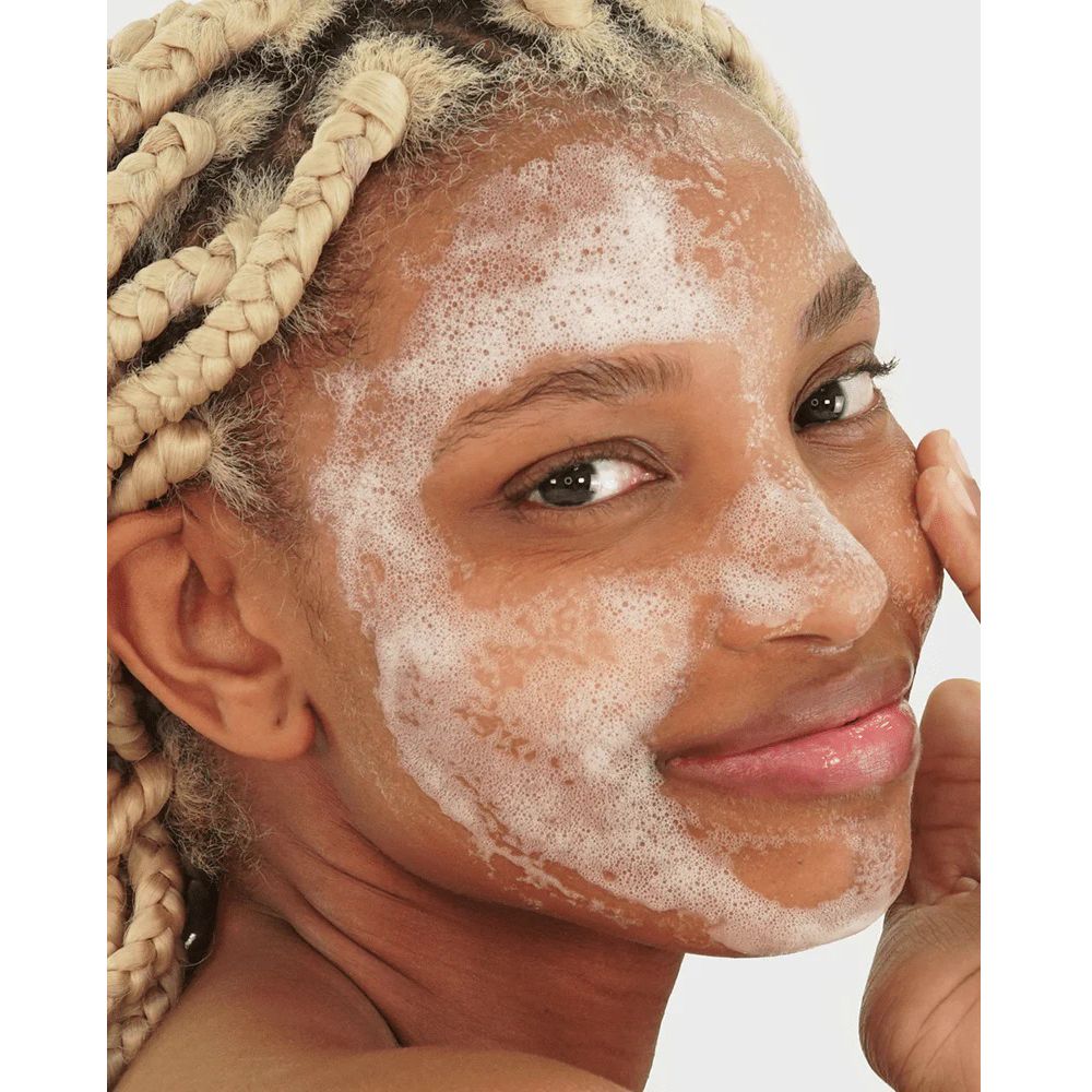 Viso di donna con trecce bionde, coperto di schiuma. Si tocca il viso.