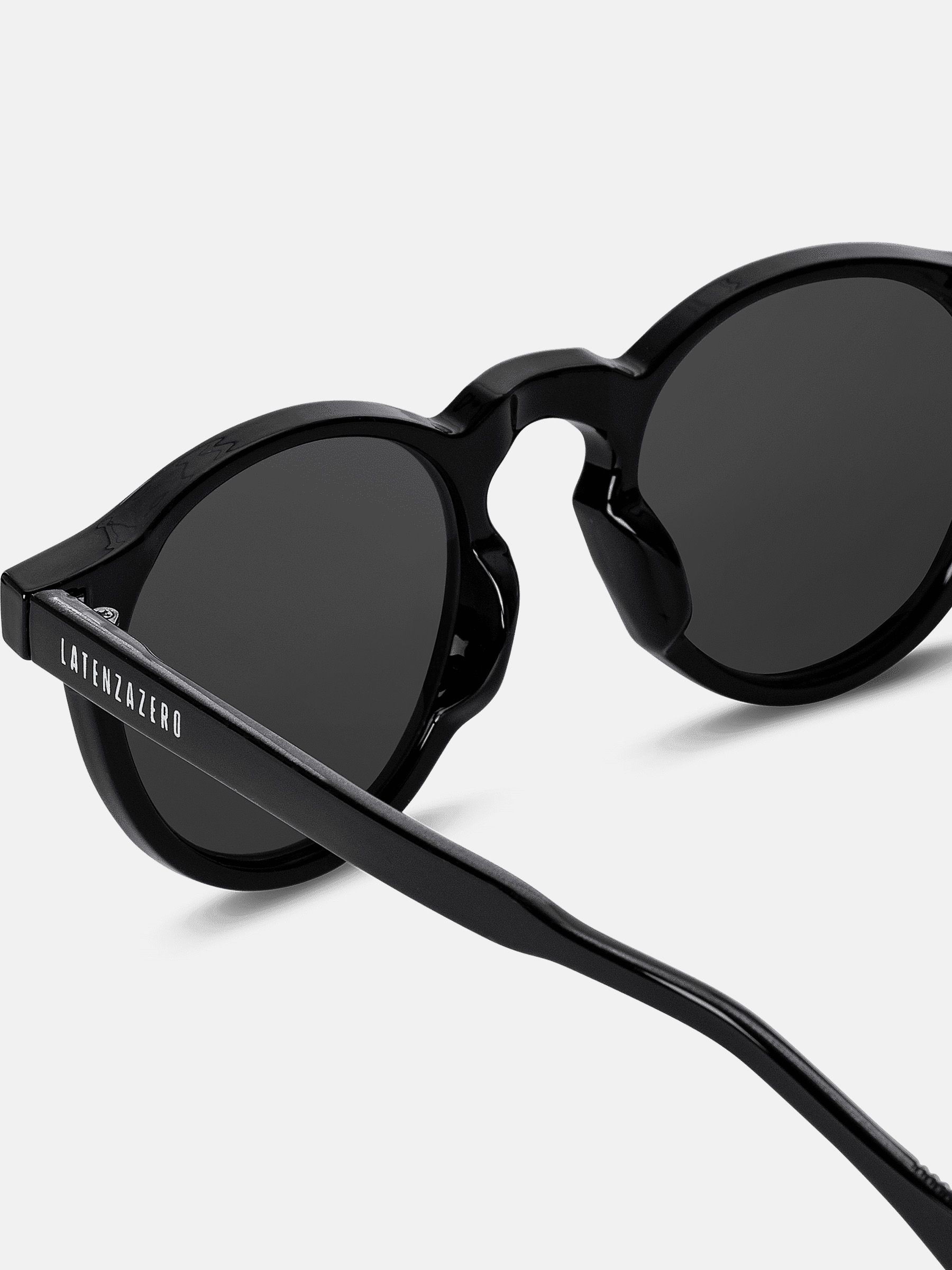 Primo piano di occhiali da sole neri con lenti rotonde. L'asta porta la scritta LATENZAZERO.