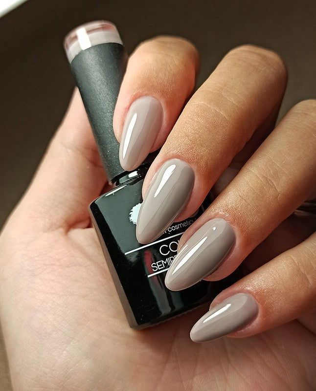 Mano con unghie smaltate Glicine dark. Flacone di smalto in mano. Unghie di forma ovale e lucide.