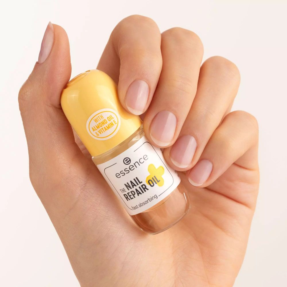Mano che tiene un piccolo flacone. Sul flacone c'è scritto "essence THE NAIL REPAIR OIL". Tappo giallo con testo.