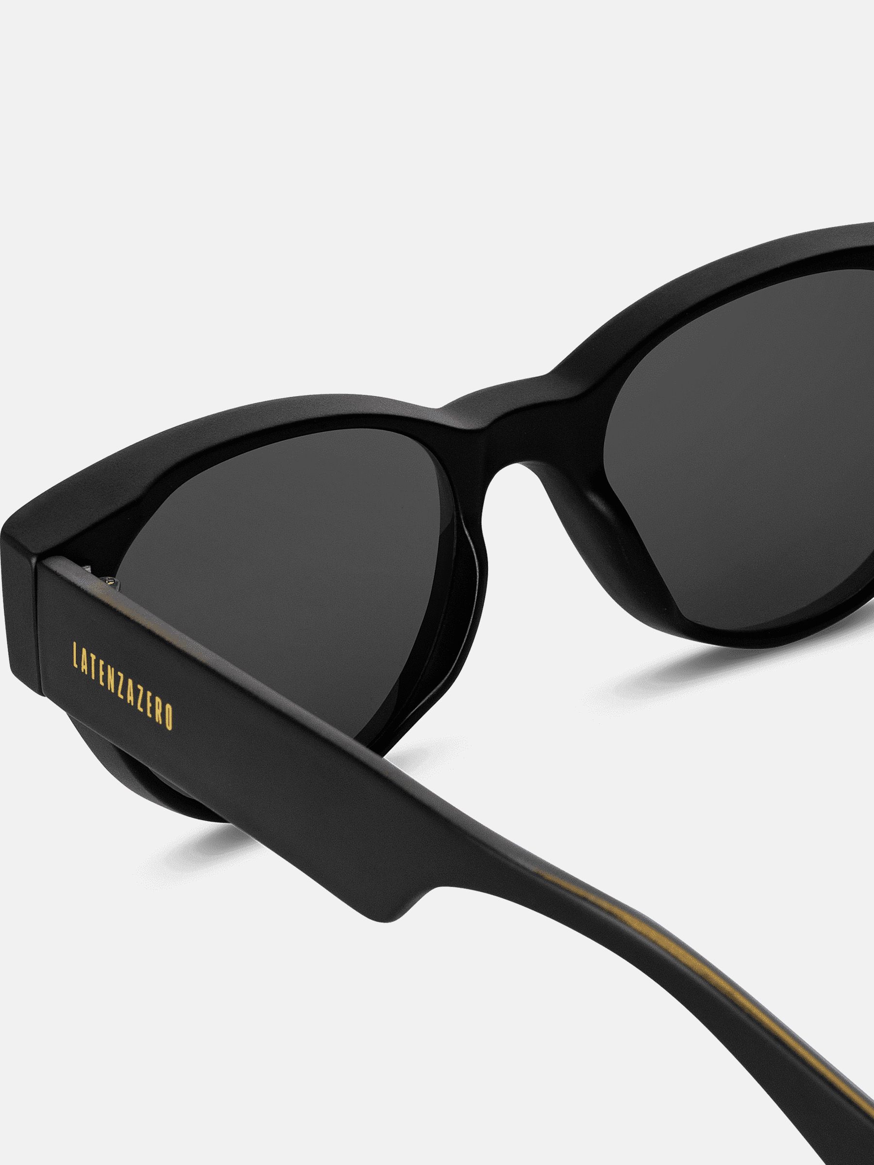 Primo piano di occhiali da sole neri. Logo Latenzazero dorato sull'asta. Lenti ovali.