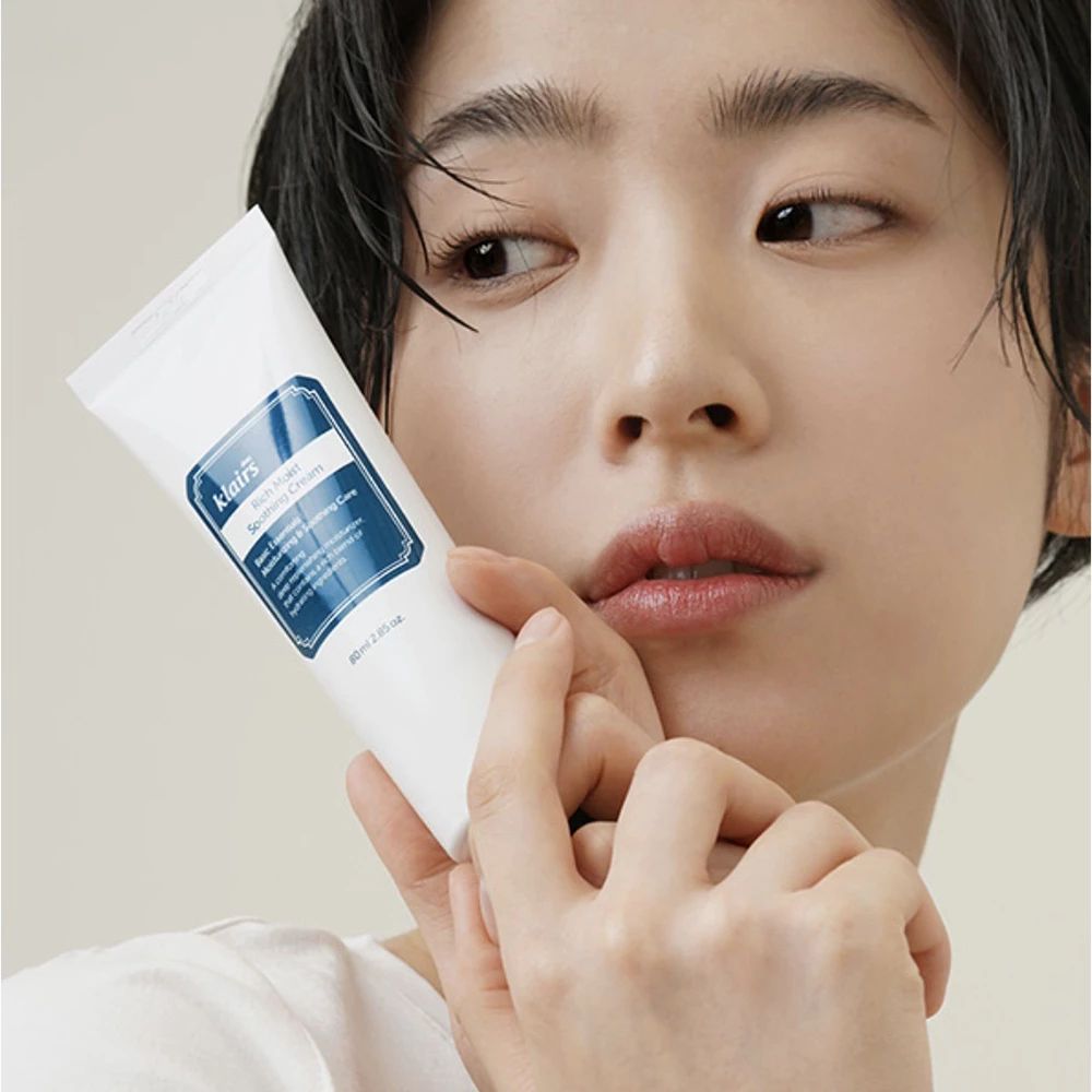 Tubo bianco con etichetta blu. Donna che tiene il tubo. Scritta: Klairs Rich Moist Soothing Cream.
