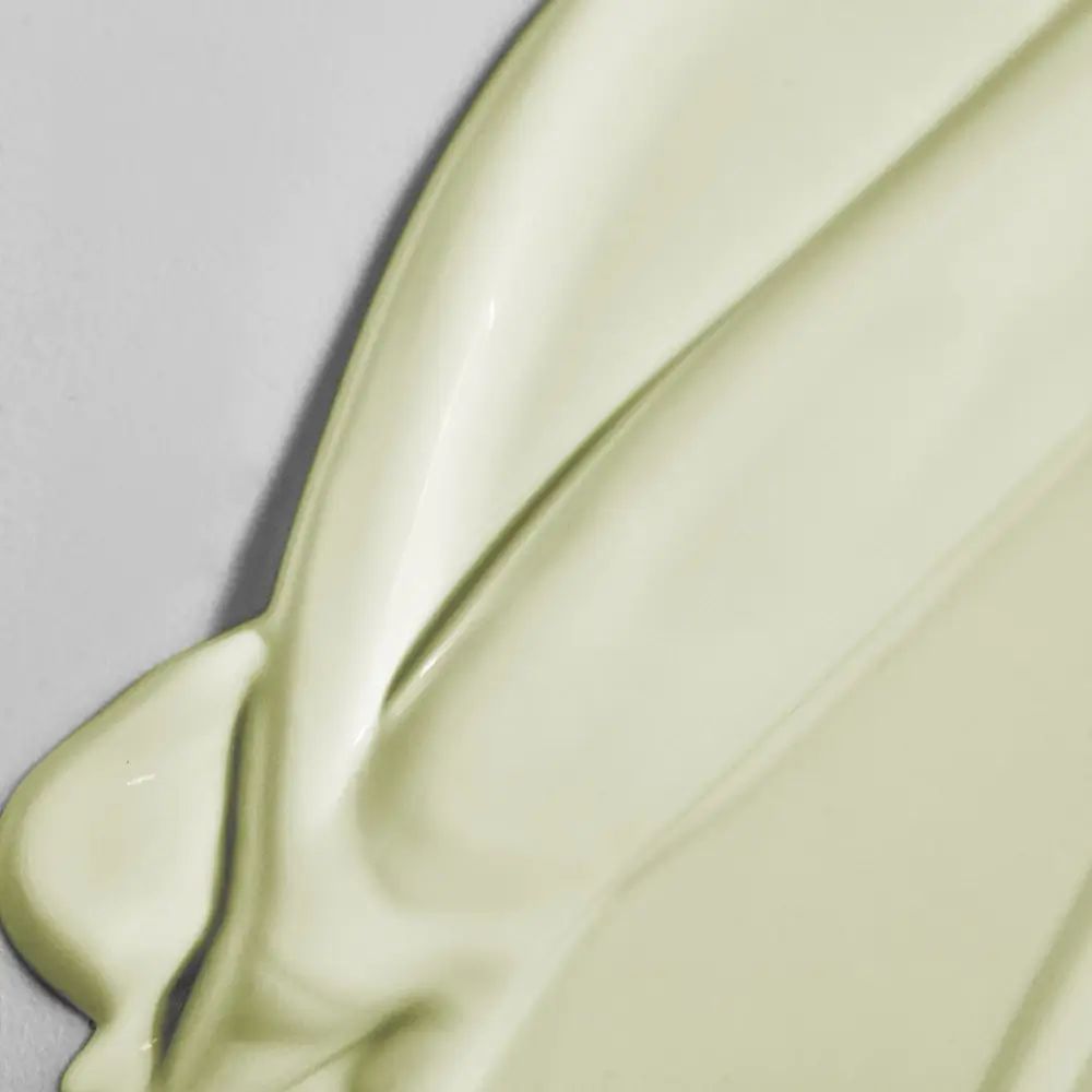 Primo piano di una texture di crema solare lucida e color crema. La texture è liscia e ondulata, distribuita su una superficie chiara.