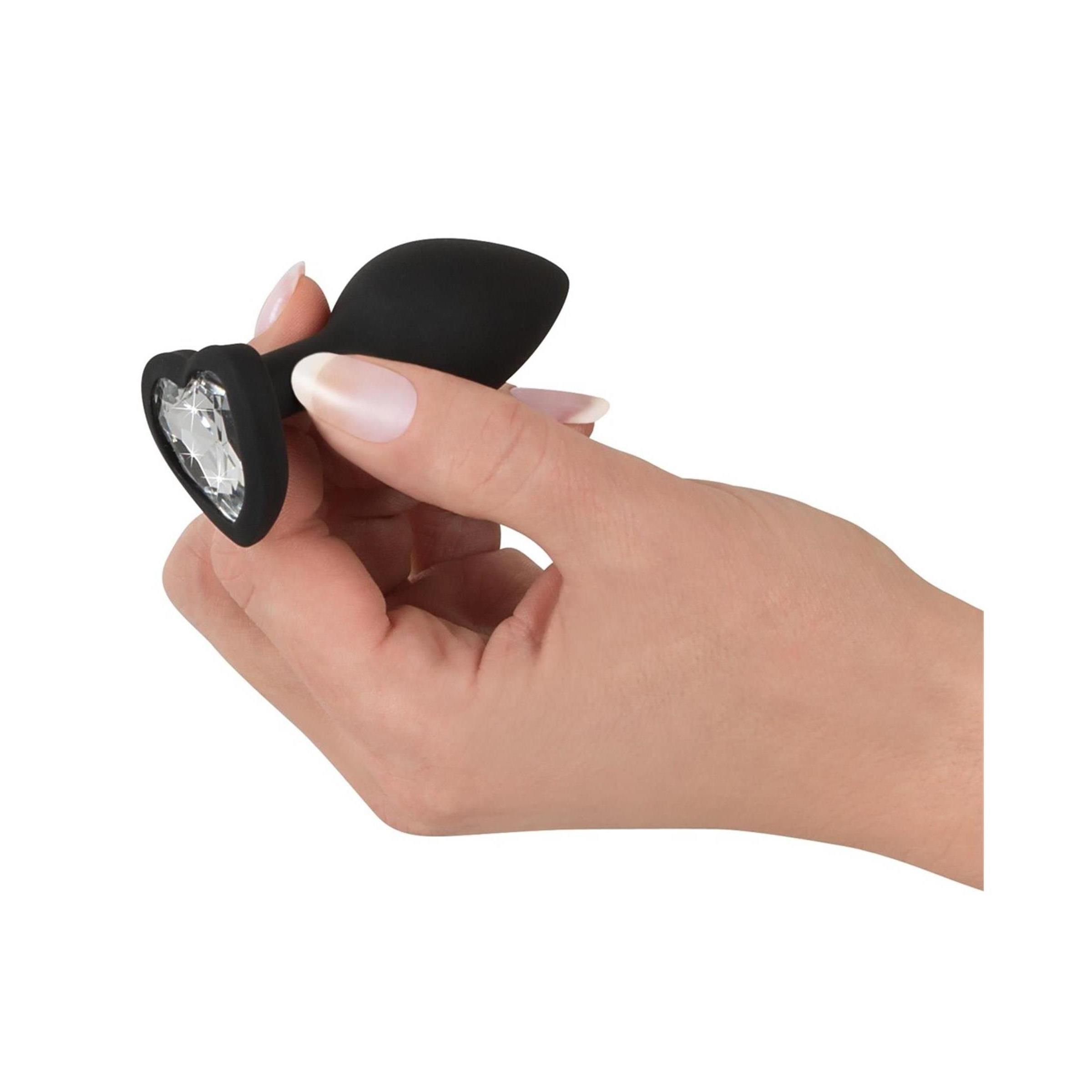 Mano che tiene un plug anale in silicone nero con decorazione a cuore in cristallo. Base a forma di cuore.
