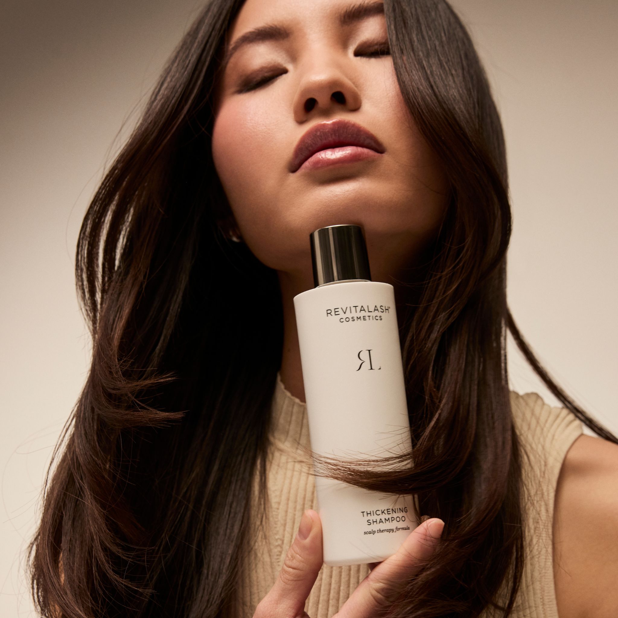 Una donna tiene una bottiglia di shampoo addensante RevitaLash davanti ai suoi lunghi capelli.