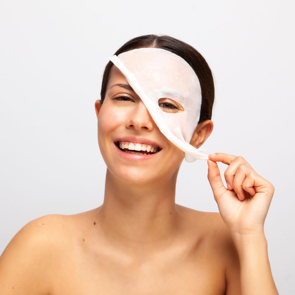 Donna che rimuove una maschera per il viso. La maschera copre occhi e naso. Sfondo chiaro.