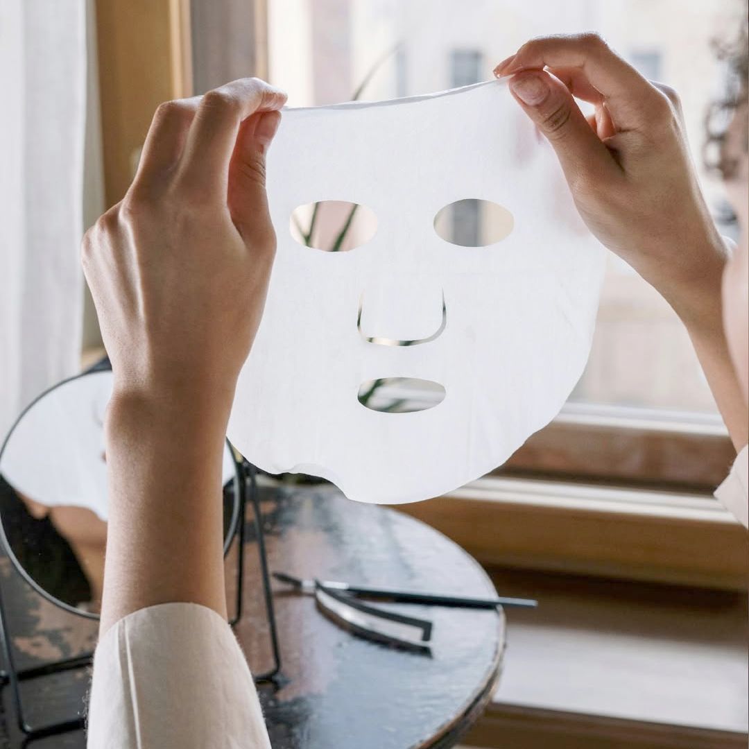 Mani che tengono una maschera facciale bianca con aperture per occhi e bocca.