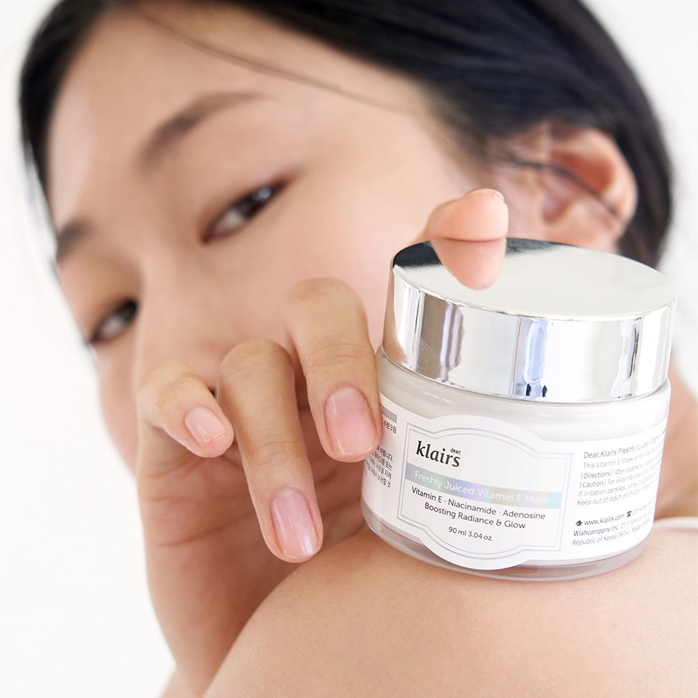 Una donna tiene in mano un barattolo della Freshly Juiced Vitamin E Mask sulla spalla.