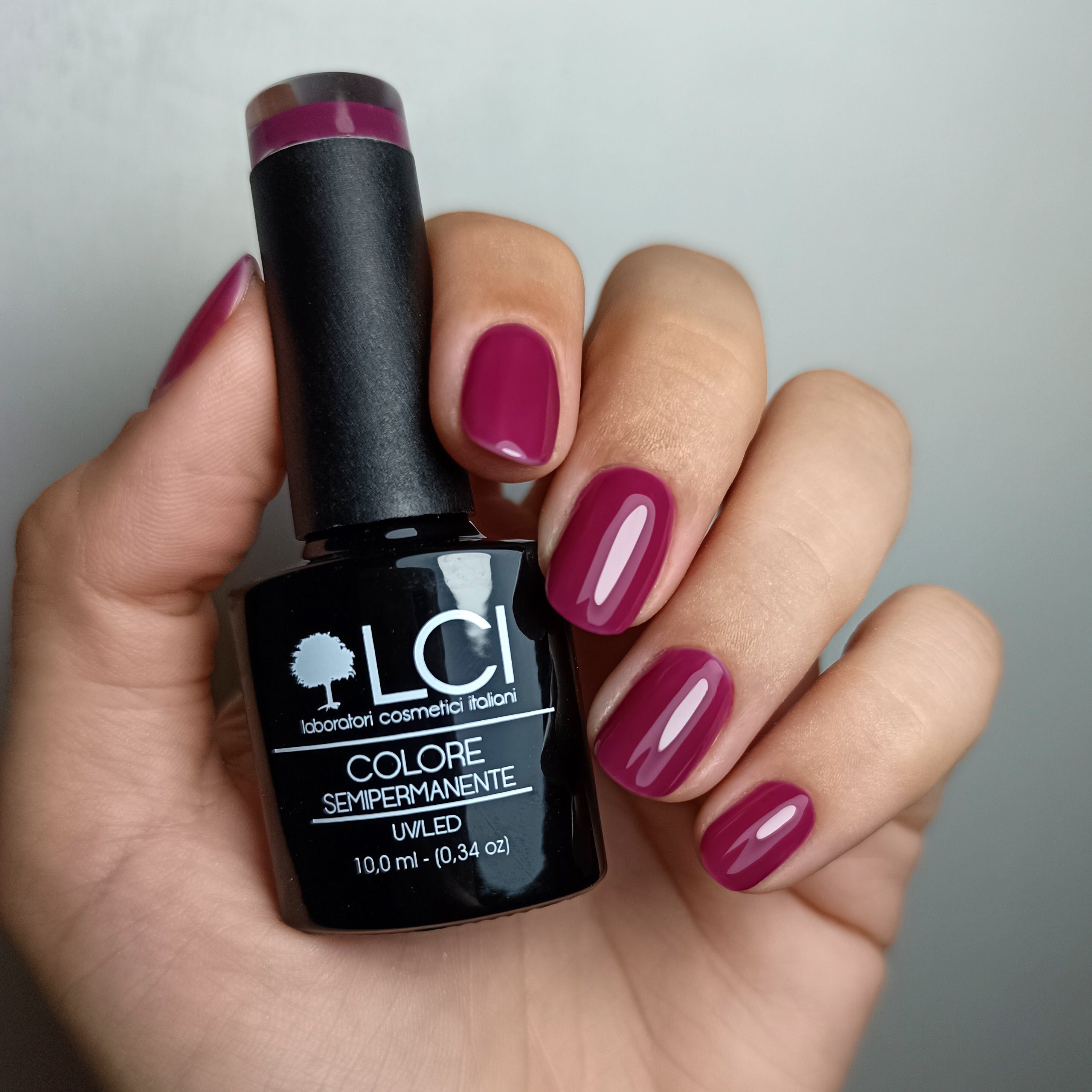 Mano che tiene un flacone di smalto e unghie smaltate di viola. Sul flacone si legge "LCI" e "COLORE SEMIPERMANENTE".