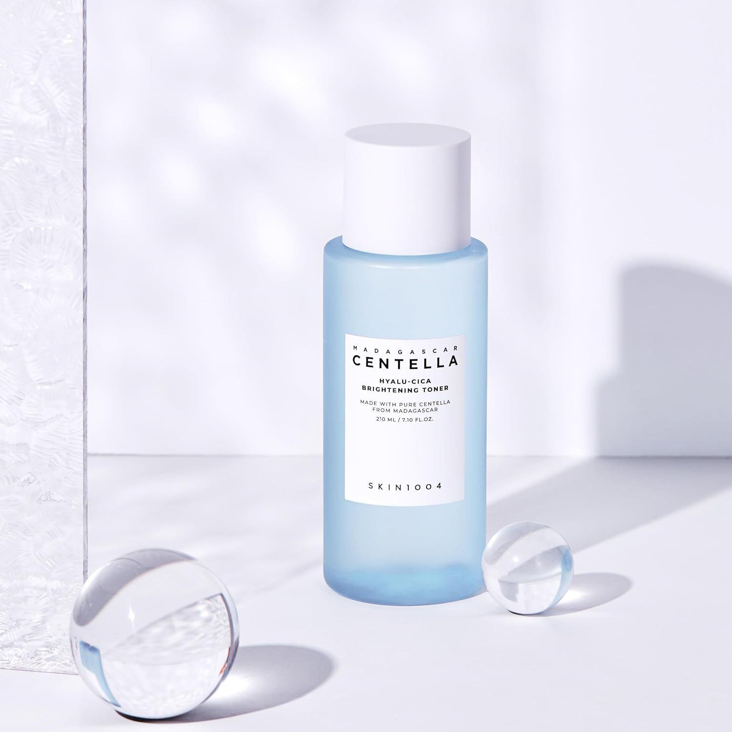 Flacone azzurro chiaro con tappo bianco. Scritta: MADAGASCAR CENTELLA HYALU-CICA BRIGHTENING TONER. Due sfere di vetro.