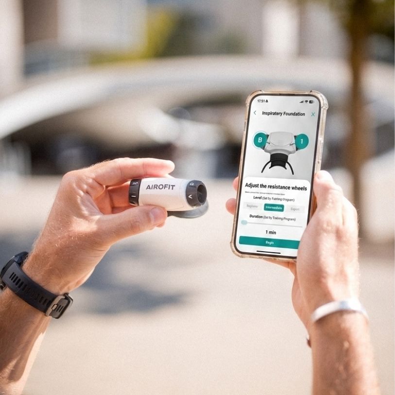 Allenatore respiratorio Airofit bianco e nero, tenuto in una mano, accanto a uno smartphone con l'app Airofit.