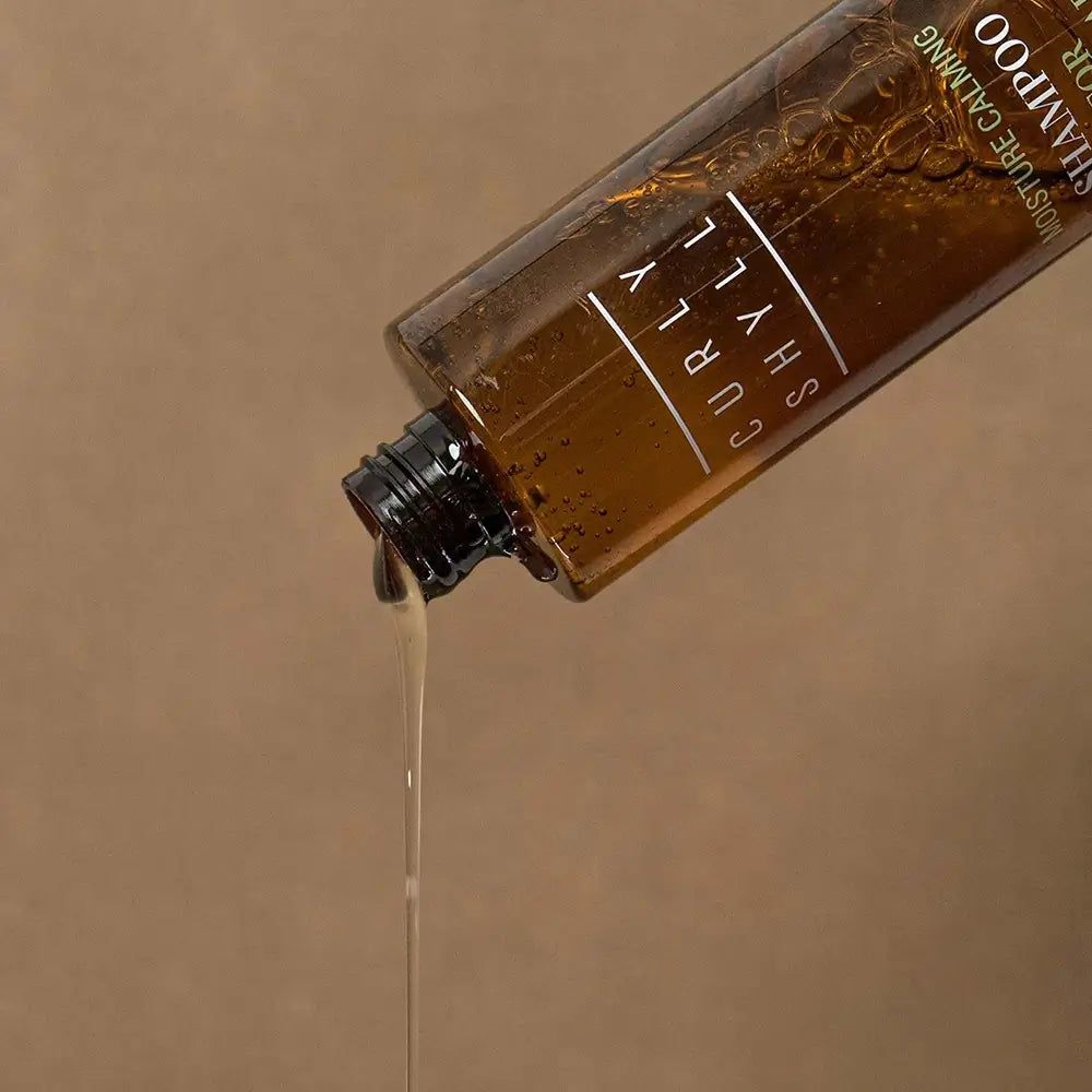 Bottiglia marrone che versa prodotto. Scritta: Curly Shyll, Moisture Calming Shampoo.