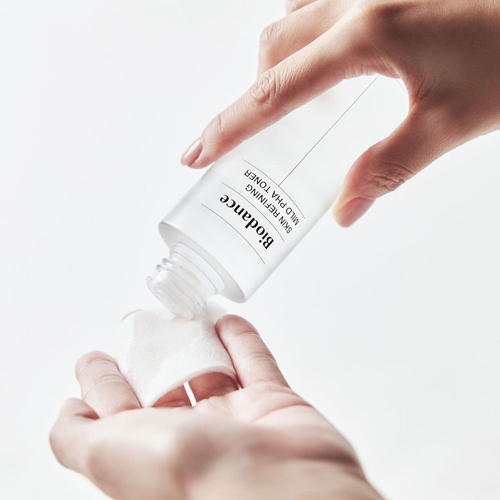Mani che tengono una bottiglia di toner Biodance e un batuffolo di cotone. Il toner viene versato.