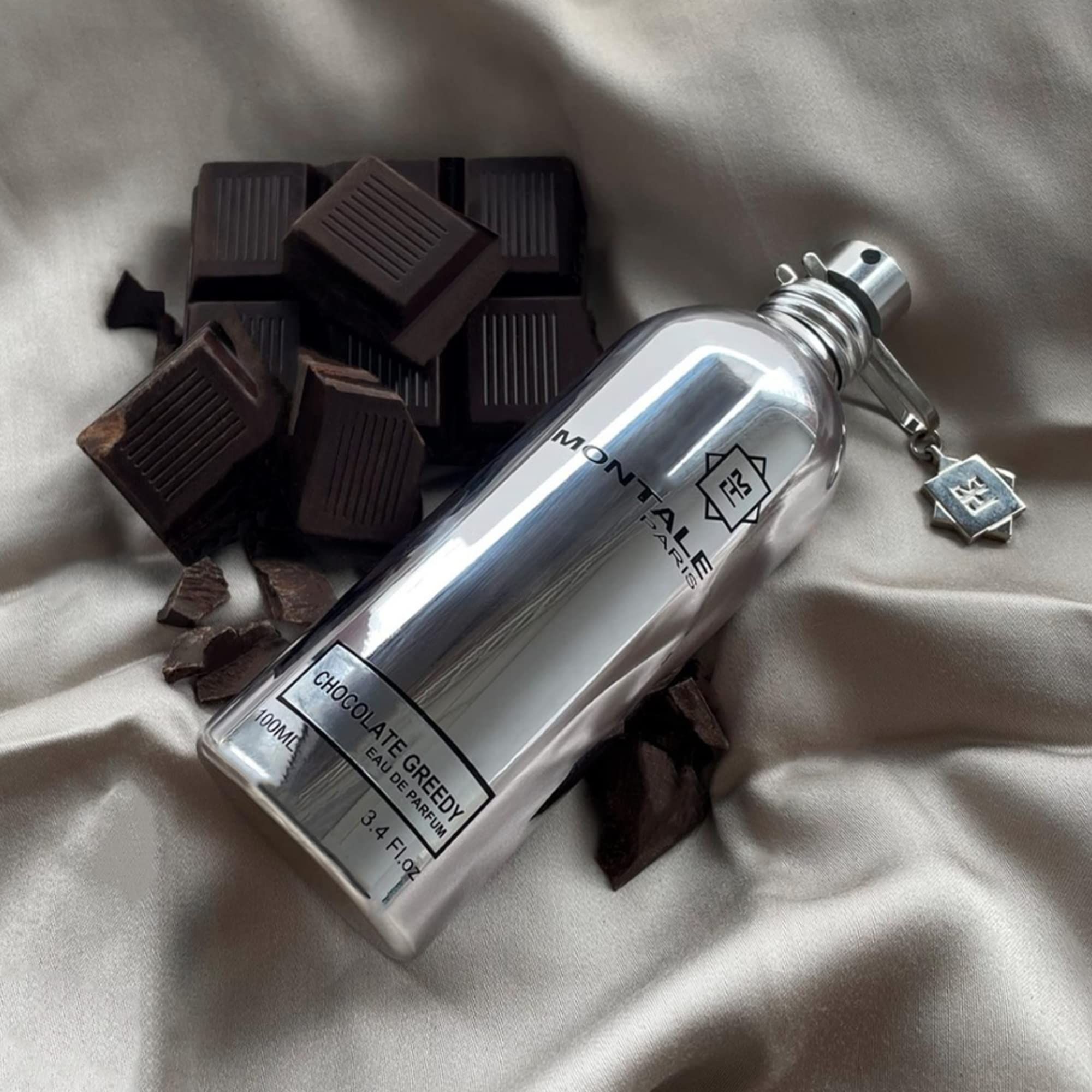 Flacone di profumo Montale Chocolate Greedy, circondato da pezzi di cioccolato su tessuto.