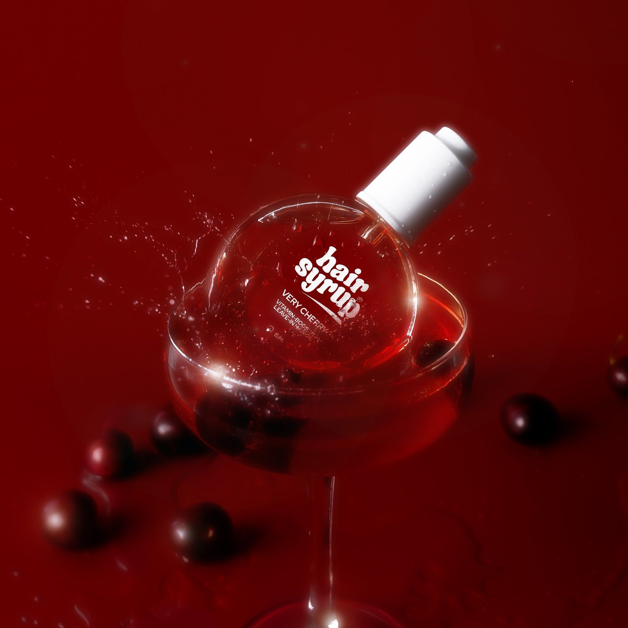 Flacone rotondo in un bicchiere da vino con liquido. Ciliegie e spruzzi. Etichetta rossa.