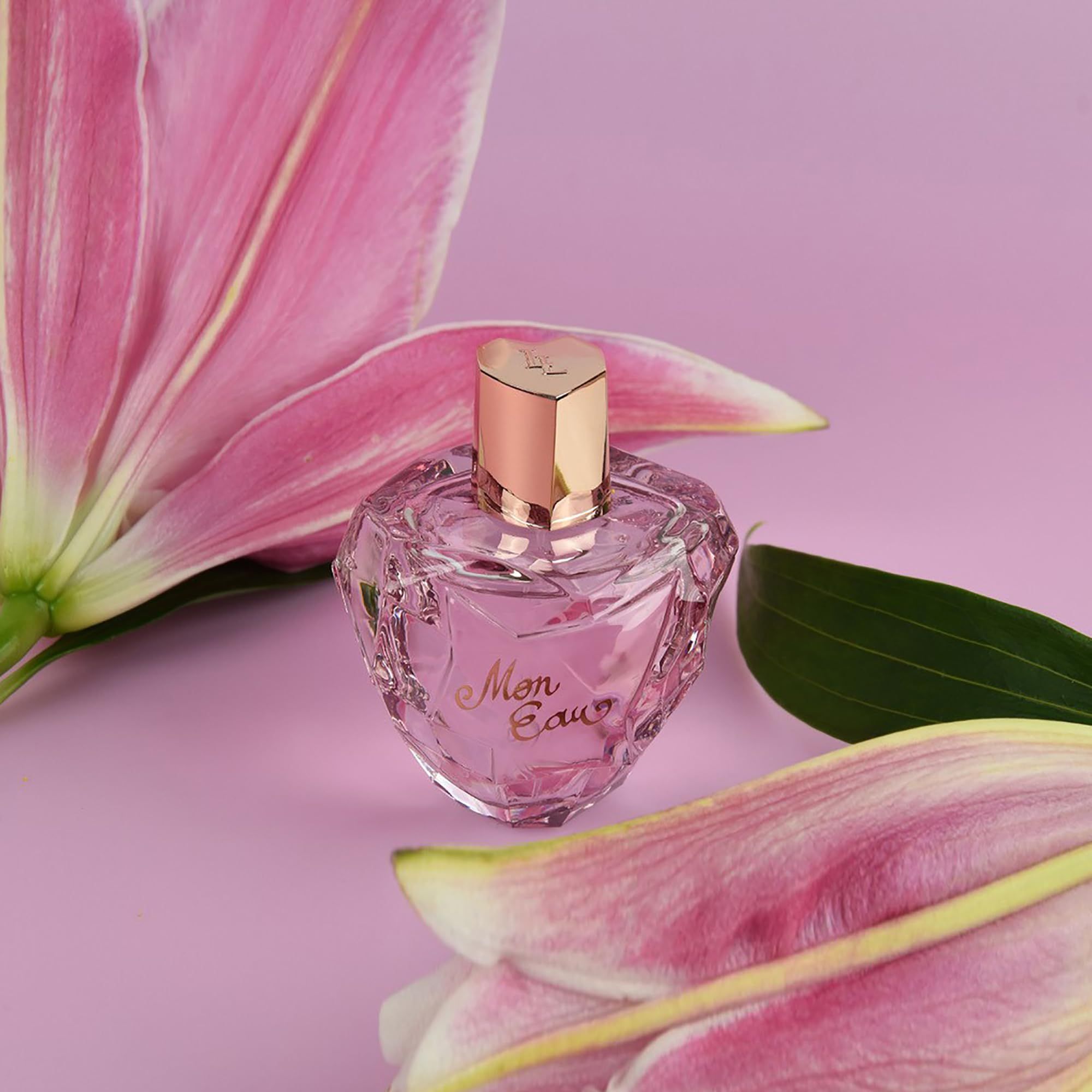 Flacone rosa con tappo dorato, circondato da fiori di giglio rosa. Scritta: Mon Eau.