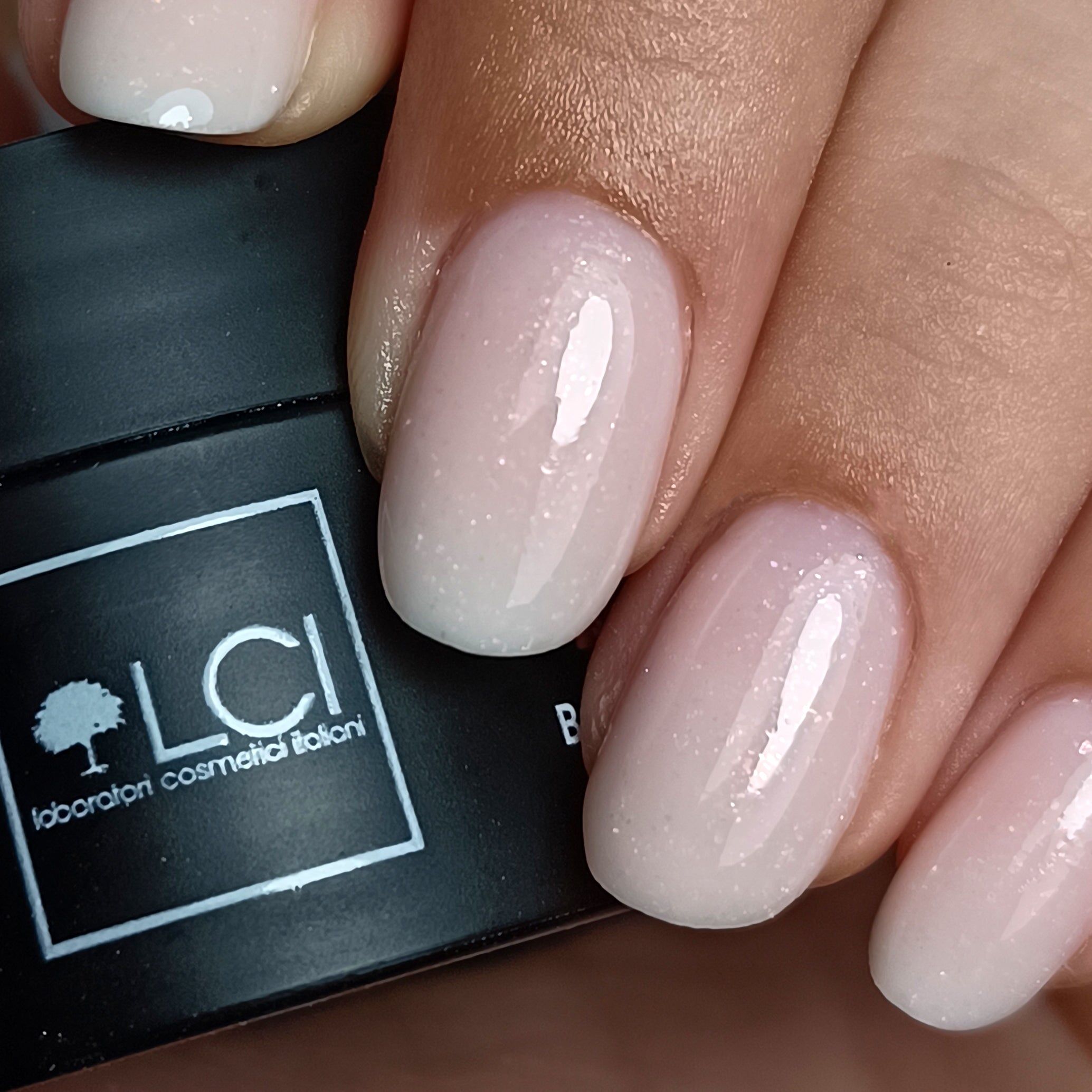 Unghie con gel costruttore rosa, glitter. Vasetto nero con logo LCI sullo sfondo.