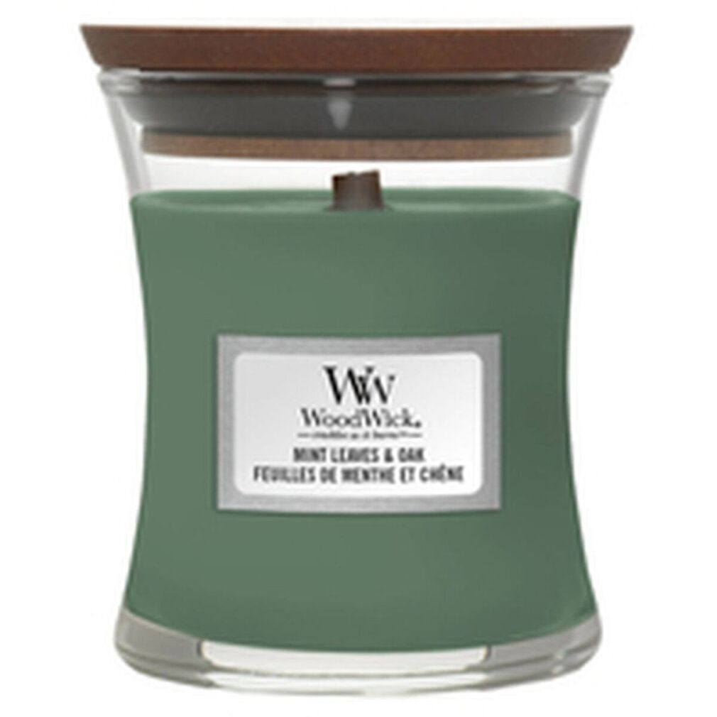 Candela verde a forma di clessidra con coperchio in legno. Etichetta con nome del prodotto e marchio WoodWick. Mint Leaves & Oak.
