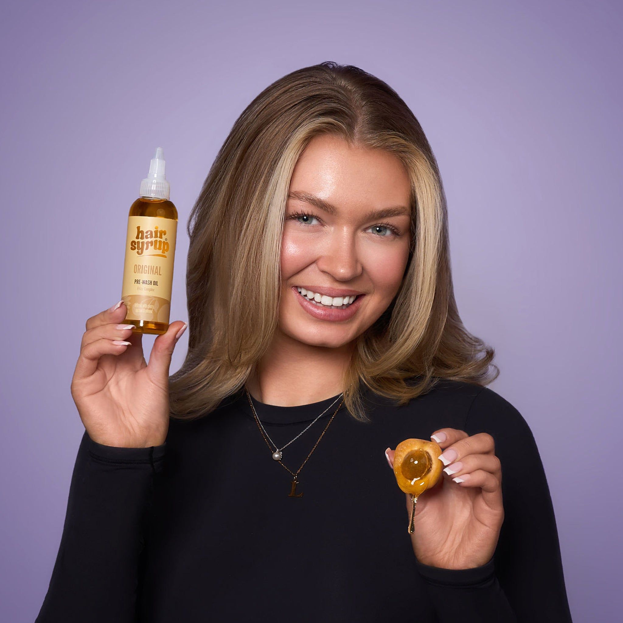 Donna che tiene in mano una bottiglia di Hair Syrup The Original e un frutto. Sorride alla fotocamera.
