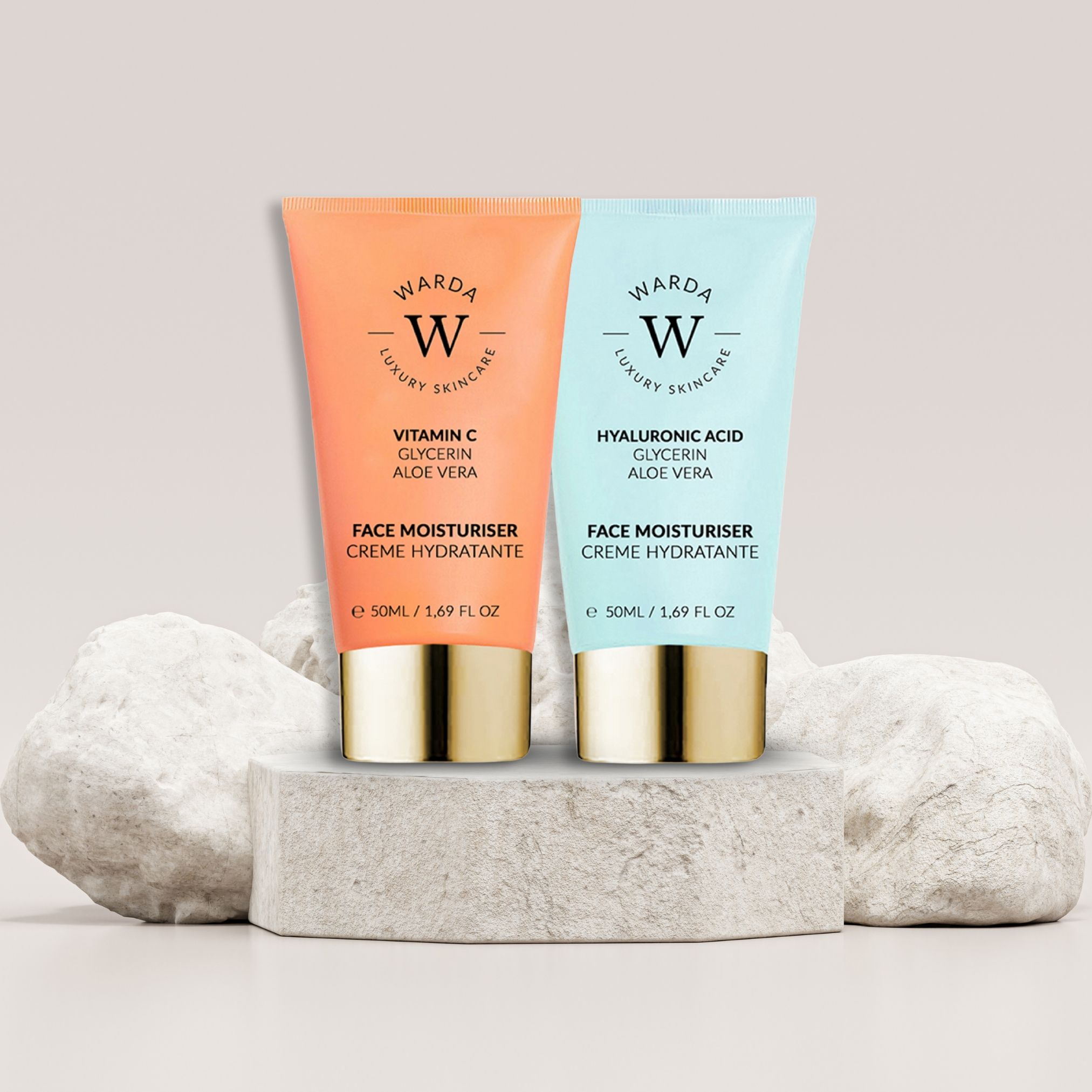 Due tubi di crema giorno Warda su un piedistallo. Tubo arancione: Vitamina C. Tubo blu: Acido Ialuronico. Tappi dorati.