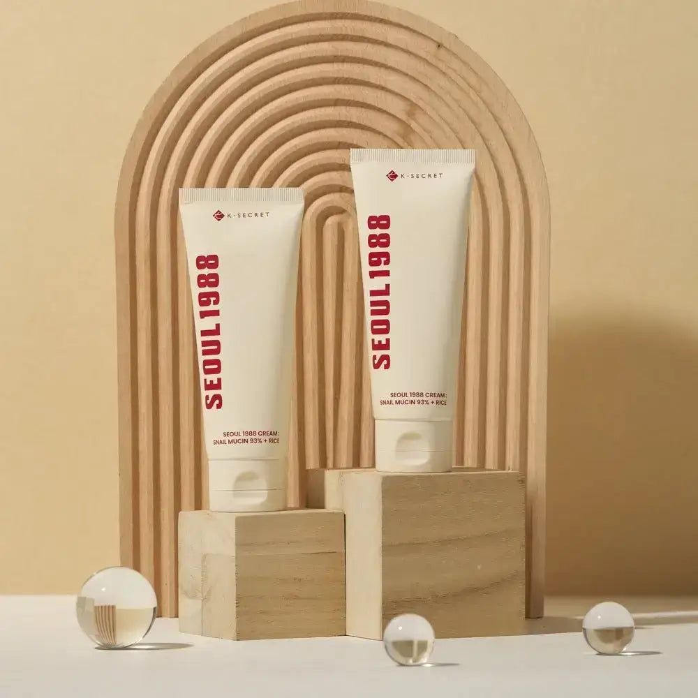 Due tubi di crema con scritta rossa SEOUL 1988. Testo: SEOUL 1988 CREAM: SNAIL MUCIN 93% + RICE. Marchio: K-SECRET.