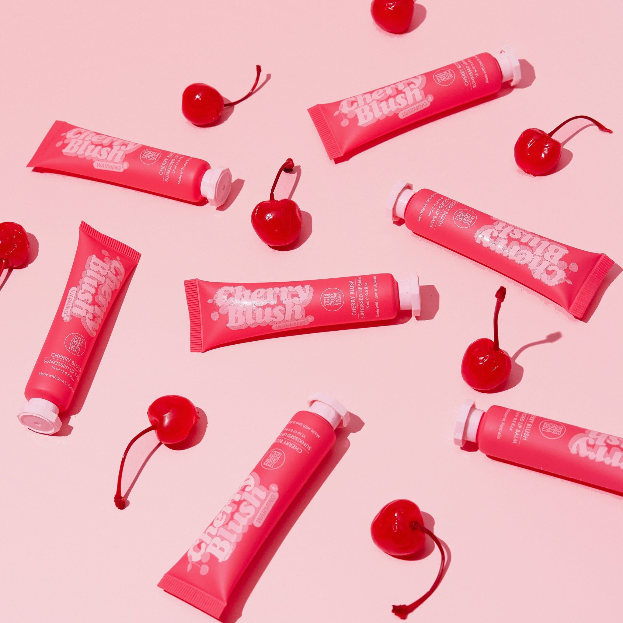 Diversi tubi 'Cherry Blush' e ciliegie su sfondo rosa. Nome del prodotto e marchio visibili.