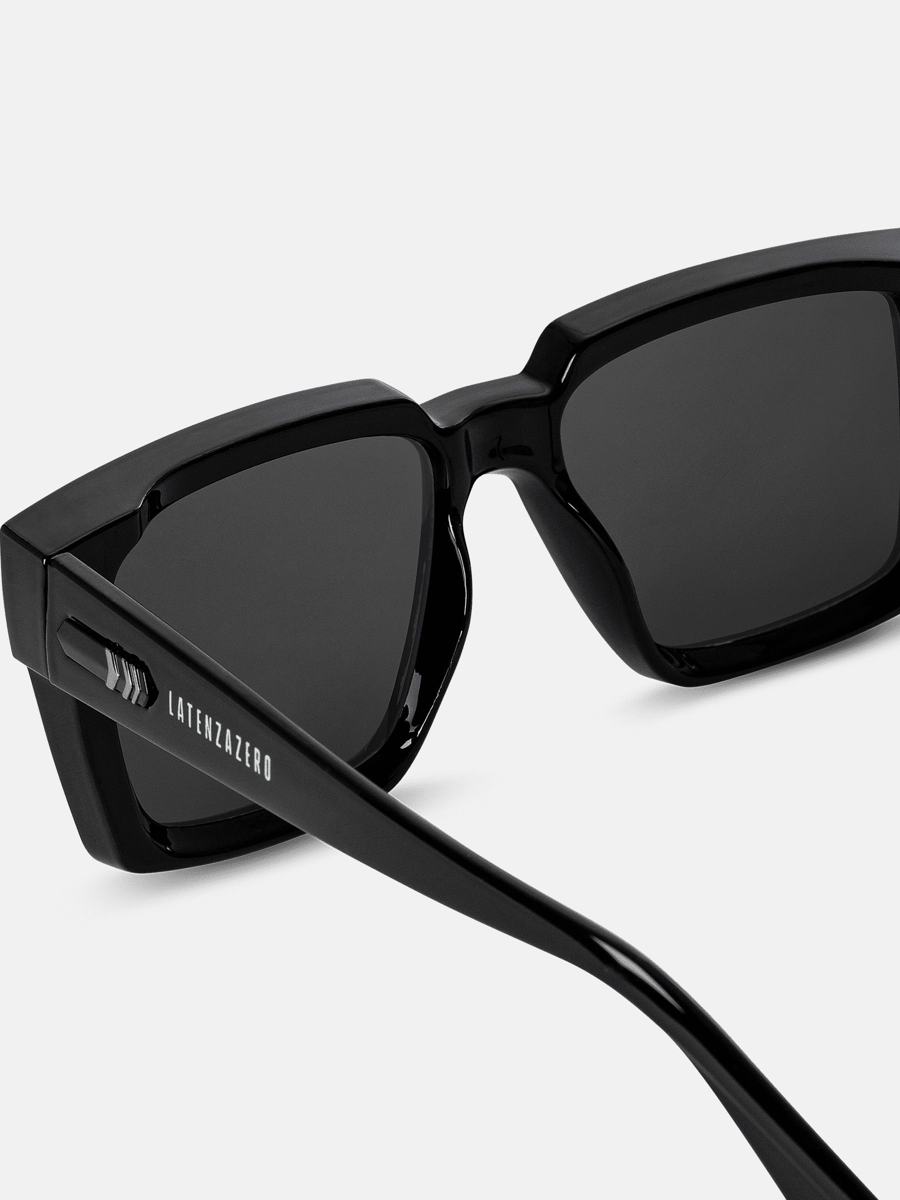 Primo piano degli occhiali da sole neri. Lenti rettangolari, montatura ampia. Logo Latenzazero sull'asta.