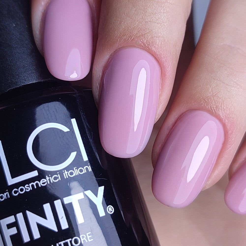 Primo piano di unghie smaltate e flacone di smalto gel. Unghie smaltate rosa pastello. Flacone nero con scritta LCI INFINITY.