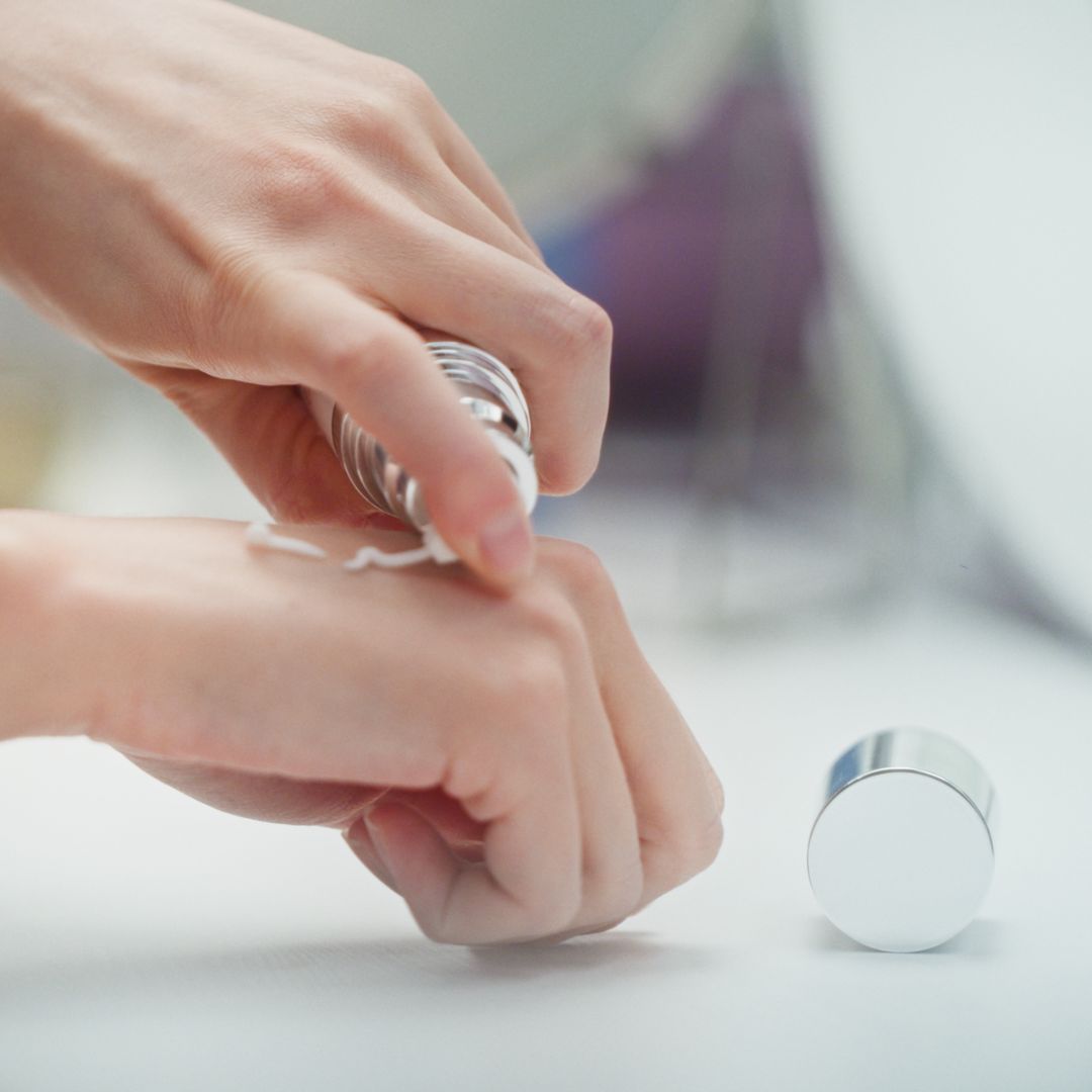 Mani applicano crema. Flacone e tappo accanto. La crema viene applicata sulla pelle.