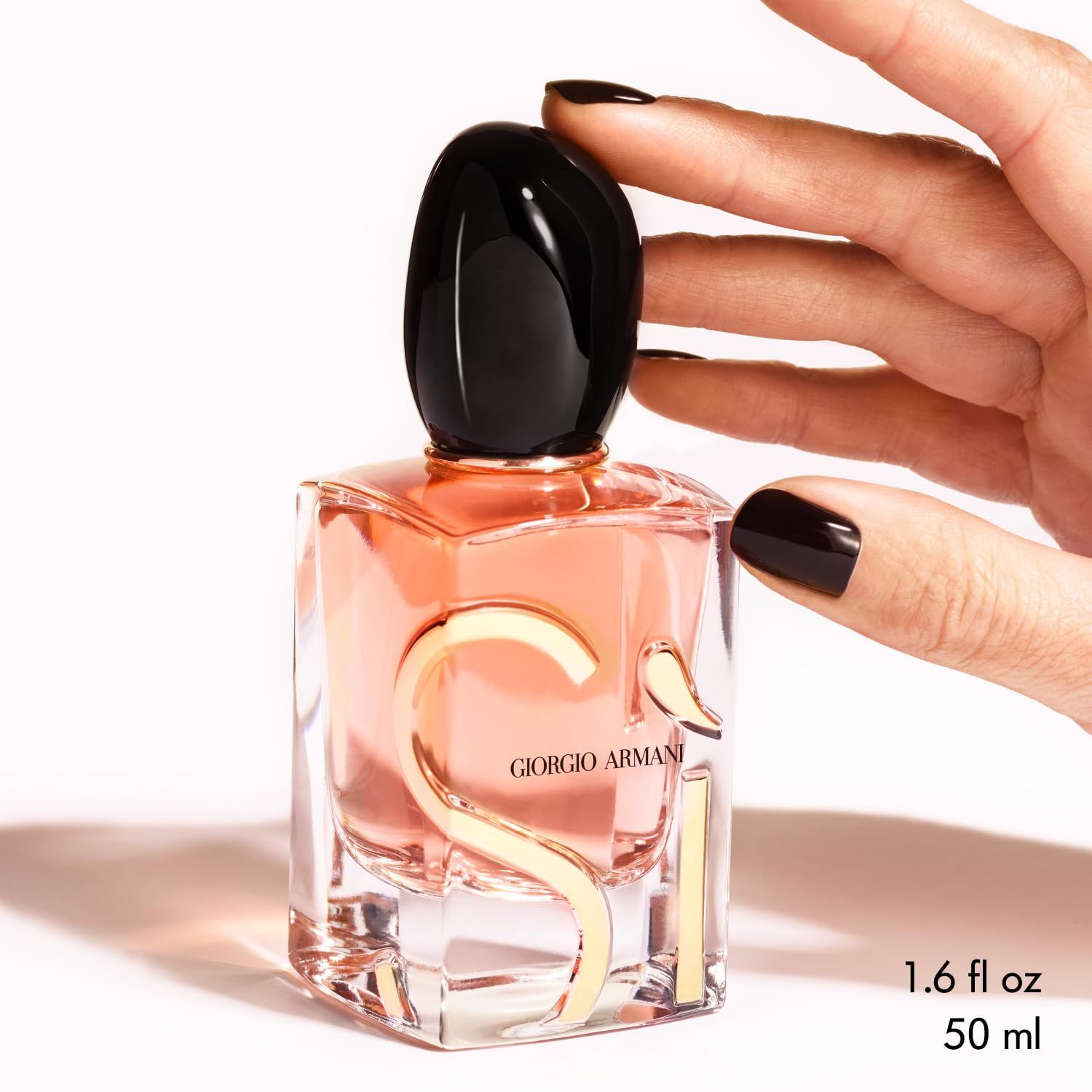 Flacone Giorgio Armani Si Eau de Parfum Intense. Lettere e dettagli dorati. Tappo nero. Liquido rosa. Mano.