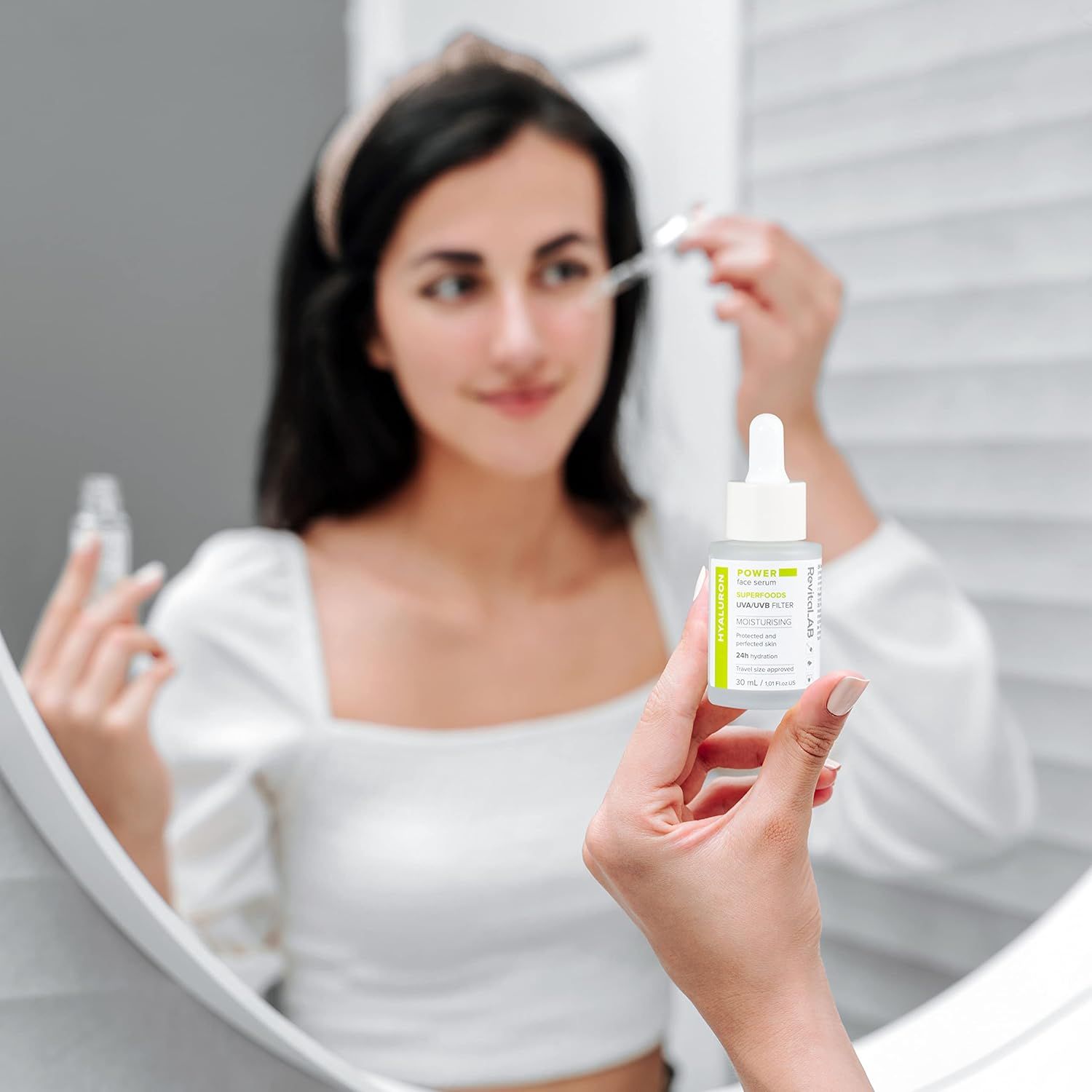 Donna tiene flacone di siero con pipetta davanti allo specchio. Informazioni sul prodotto visibili. Marchio RevitaLAB.