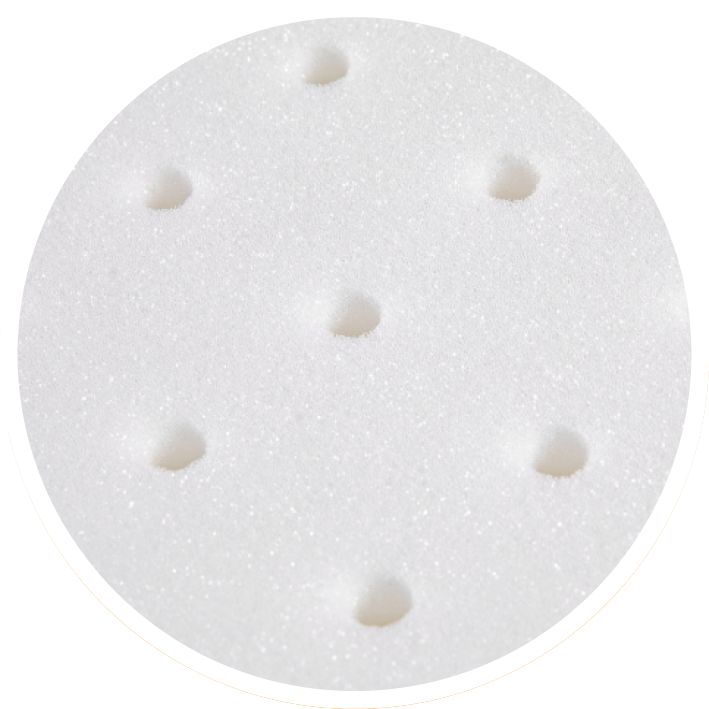 Primo piano di una superficie in schiuma bianca con sei fori circolari. La superficie è porosa.