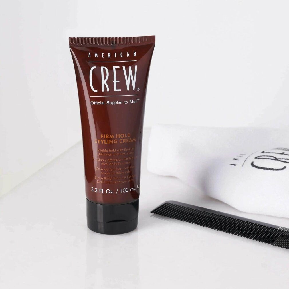 Tubo marrone con tappo nero. Scritta: American Crew, Firm Hold Styling Cream. Accanto, pettine e asciugamano.