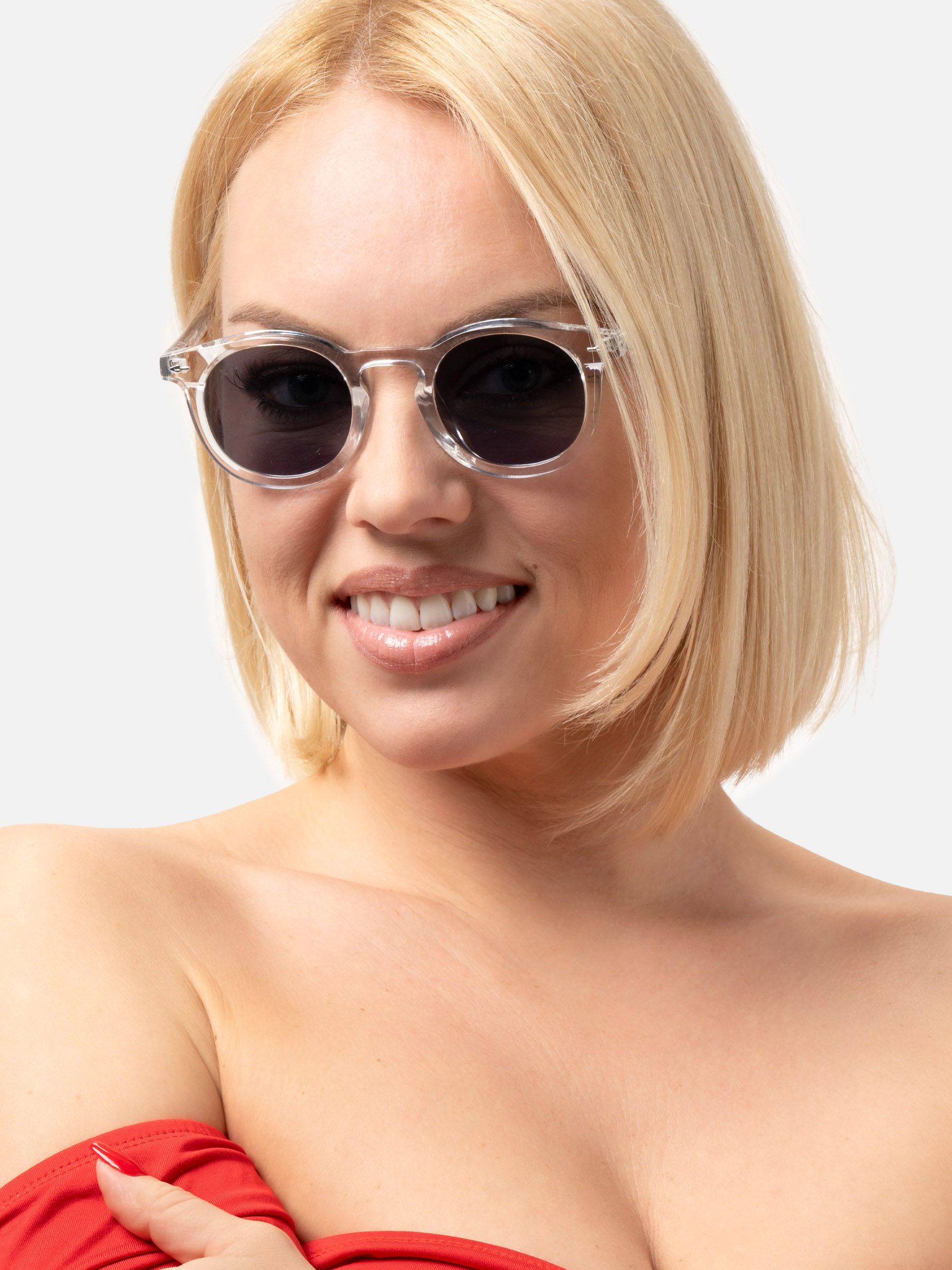 Donna con occhiali da sole rotondi, montatura trasparente, lenti scure. Primo piano, sorridente.