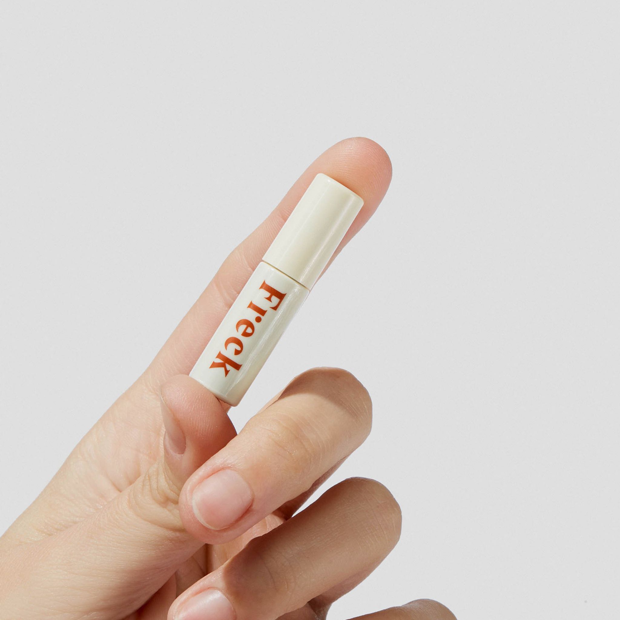 Flacone con scritta rossa "Freck", tenuto da una mano. Tappo bianco. Su sfondo chiaro.
