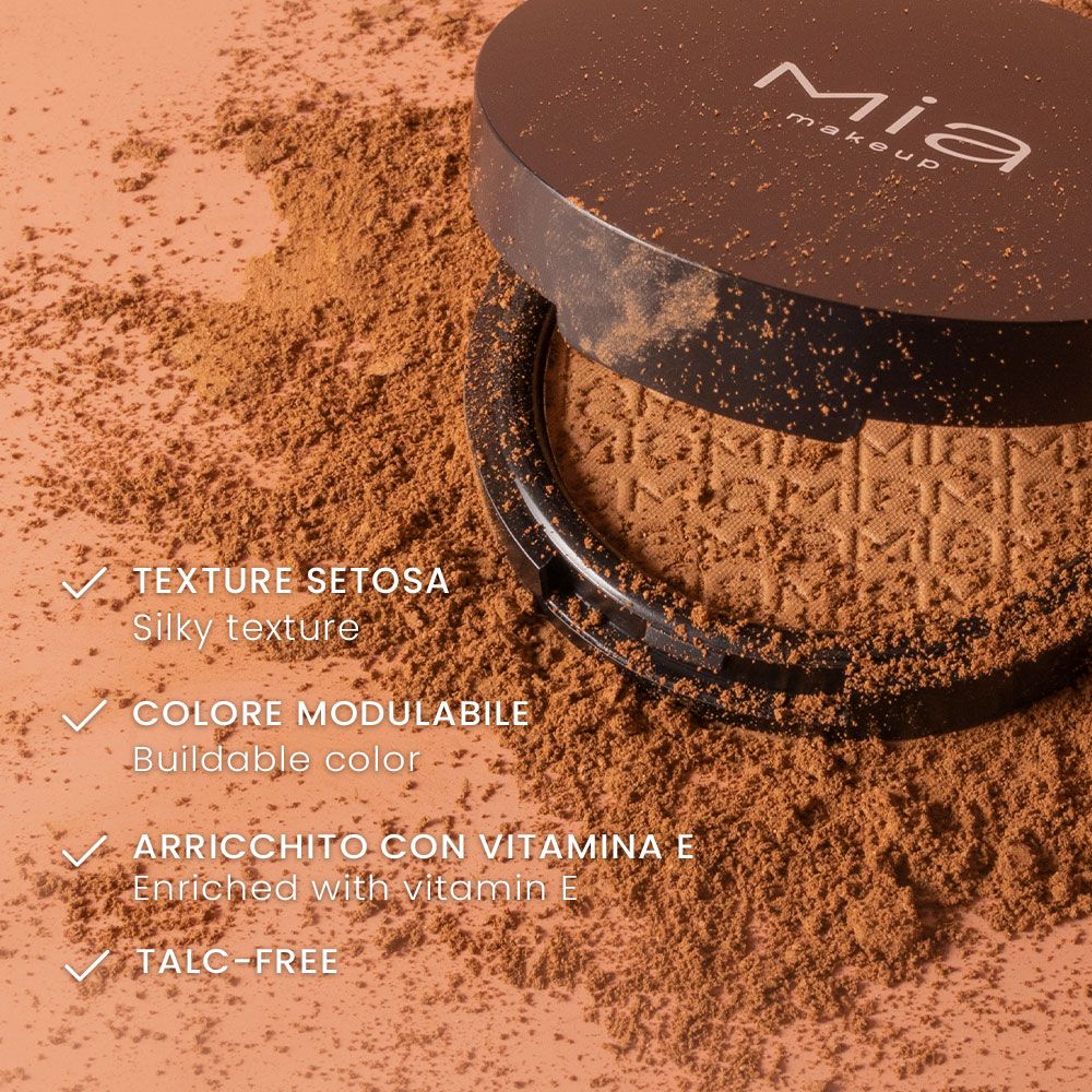 Primo piano di un contenitore cosmetico aperto con polvere marrone. Parole chiave: texture setosa, colore modulabile, arricchito con vitamina E.