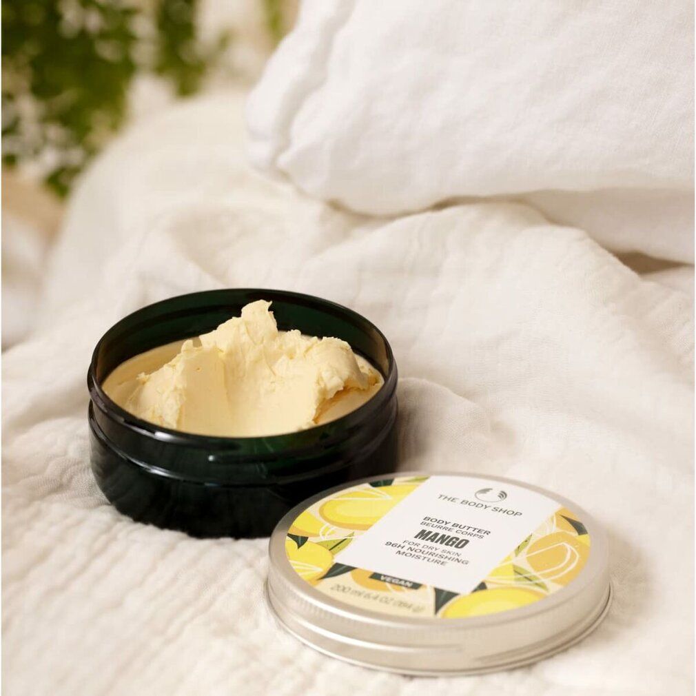 Barattolo aperto di Body Butter Mango, accanto al coperchio. Su tessuto bianco. Scritta: Body Butter Mango, per pelle secca, idratazione 96h.