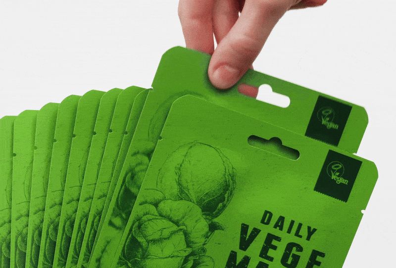 Diverse maschere viso verdi con scritta "DAILY VEGE MASK". Una mano afferra una maschera. Logo vegano.