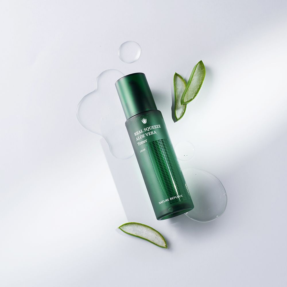 Flacone verde di toner all'aloe vera, circondato da foglie e liquido su sfondo bianco.