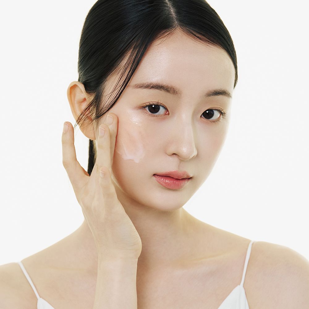 Giovane donna con cura della pelle. Viso e mano. Prodotto applicato. Pelle chiara, top bianco.