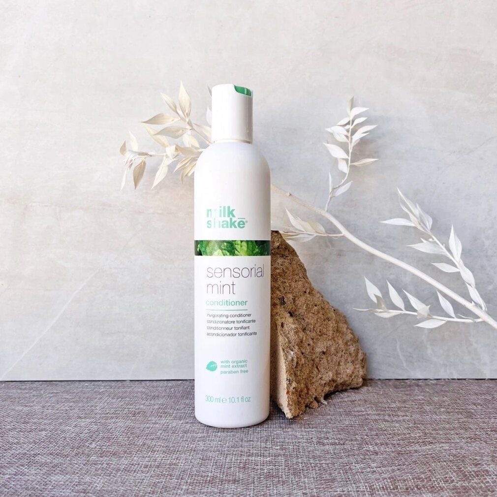 Flacone bianco con stampa verde. Scritta: milk_shake, sensorial mint conditioner. Contiene estratto di menta. Volume: 300 ml. Su pietra e decorazioni.