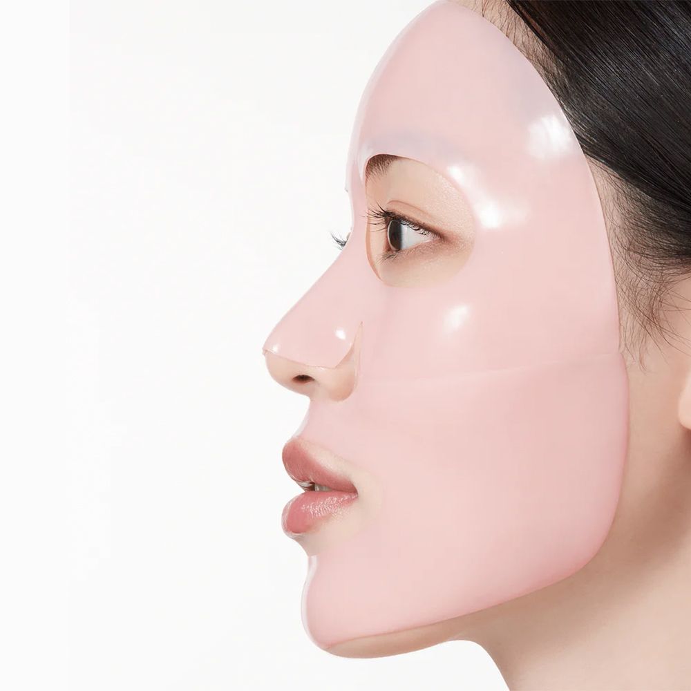 Viso di donna con maschera collagene illuminante Anua Peach 70 Niacin. Maschera rosa che copre il viso.